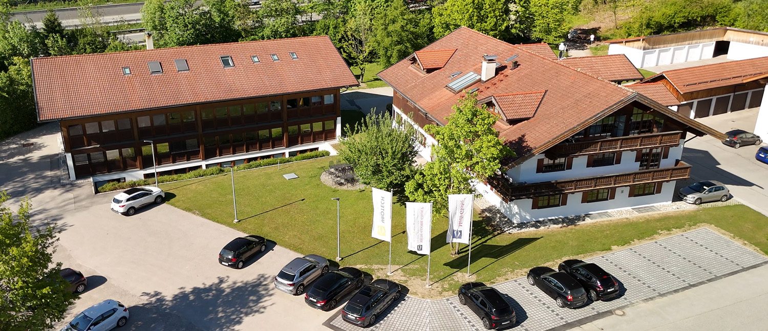 Luftaufnahme des Unternehmensgebäudes von mediglobe - urovision. Zwei große Häuser im klassisch bayerischen Stil mit grüner Weise und Parkplatz davor