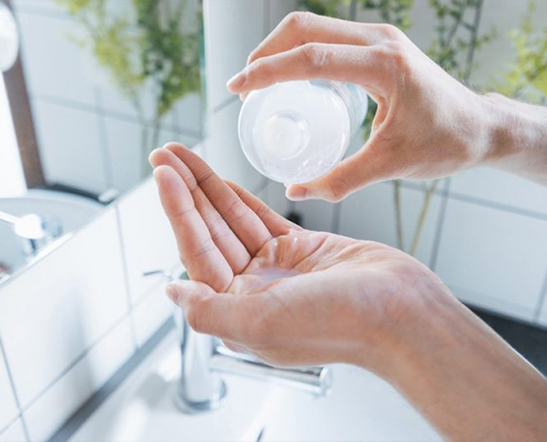 Eine Frau gießt Seife auf ihre Hand über dem Waschbecken. Das Helle, saubere Bad und das helle Licht im Hintergrund vermittelt hygiene und wohlbefinden.